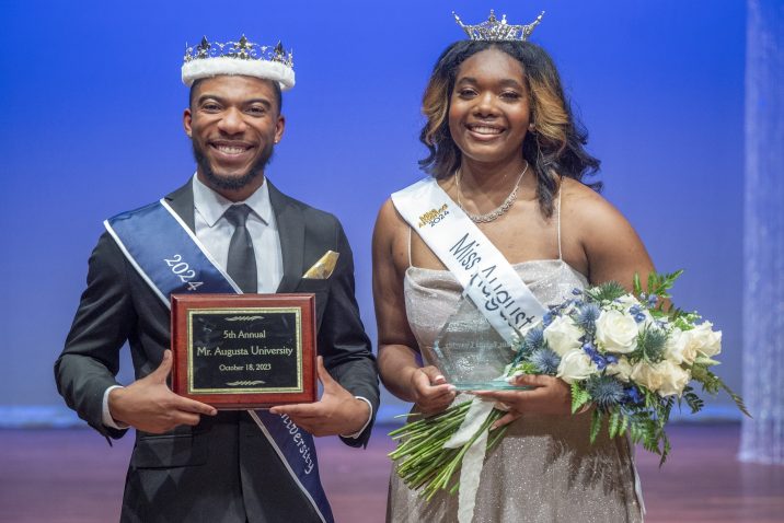 a man in a suit is crowned Mr. Augusta University and a woman in a ballgown is crowned Miss Augusta University