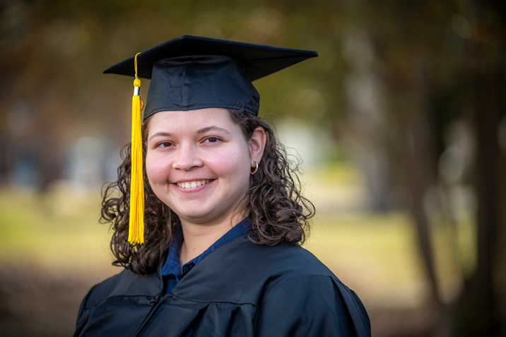 woman wearing a graduation cap and gown smiling outside