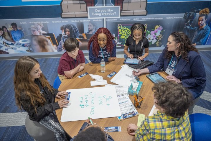 Four students sit around a table with two women from Augusta University in the Augusta University storefront at the Junior Achievement Discovery Center.