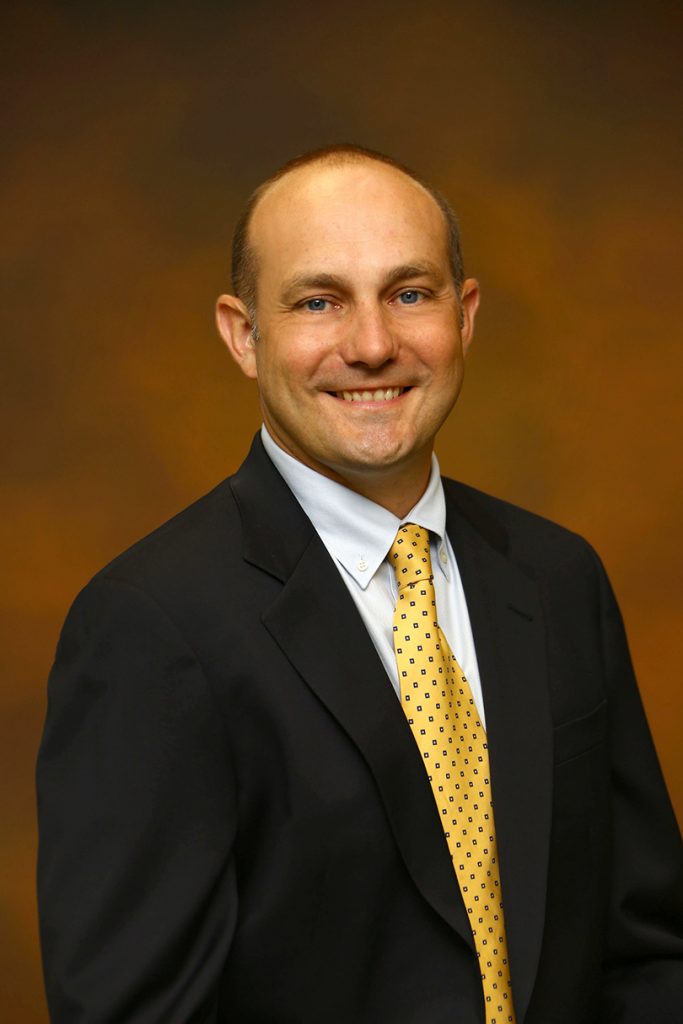 man in black suit with yellow spotted tie, smiling