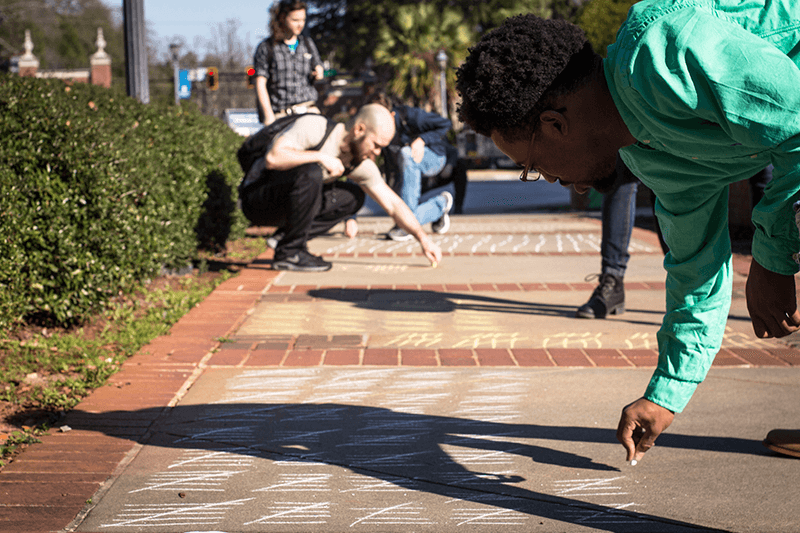 student chalks a sidewalk