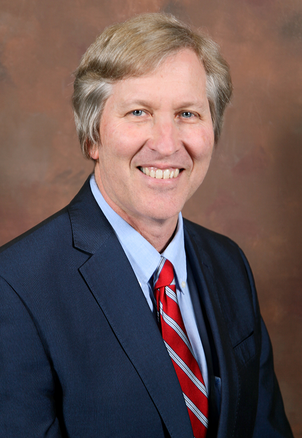 man in suit and tie smiling for a picture in front of a textured background