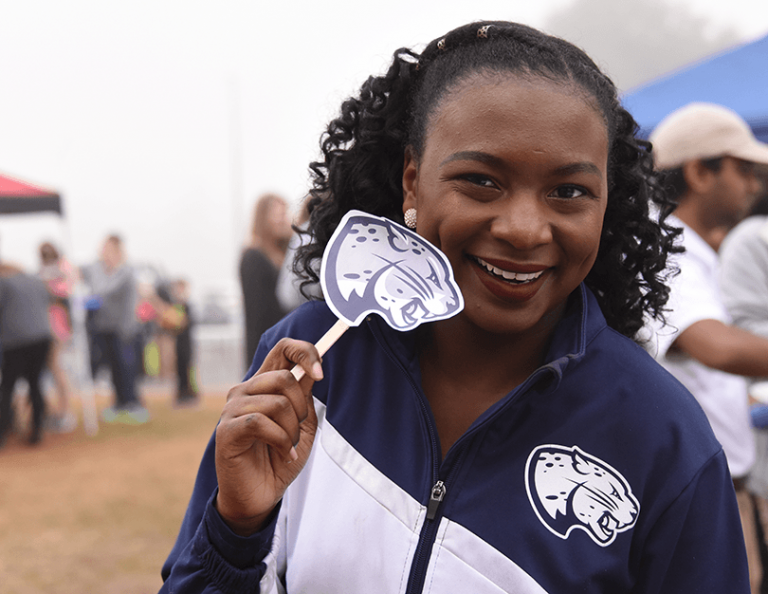 A lady holding a sign of Augusta University Jaguar head.