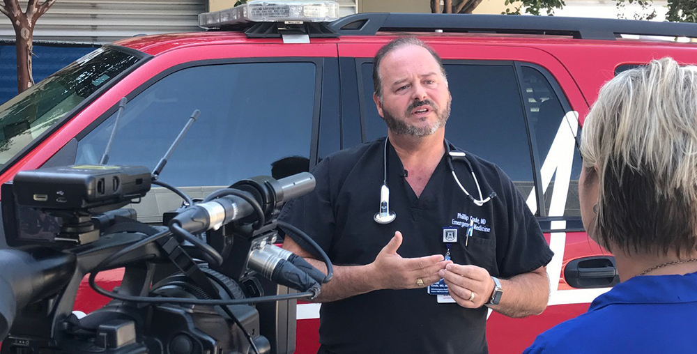 A man in hospital scrubs being interviewed by the media.