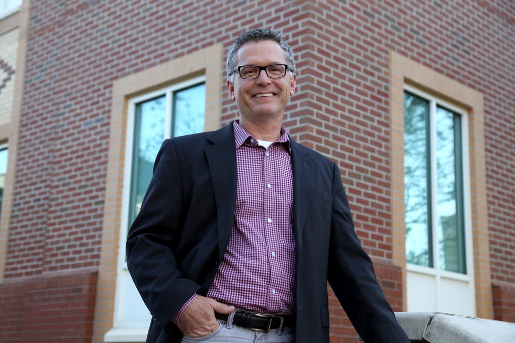 man with glasses standing outside of building, smiling 