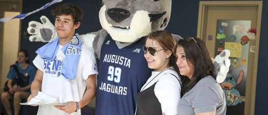 Mascot posing with a two women and a man.