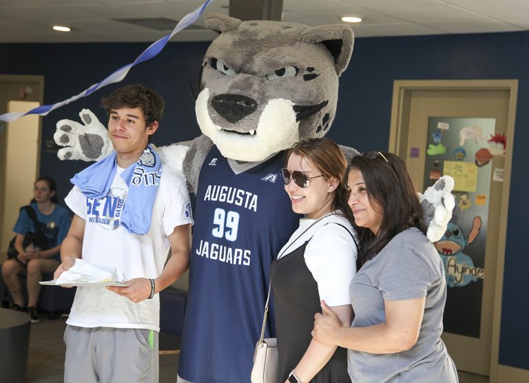 Mascot posing with a two women and a man.