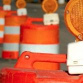 A line of orange and white construction barrels with orange lights on top