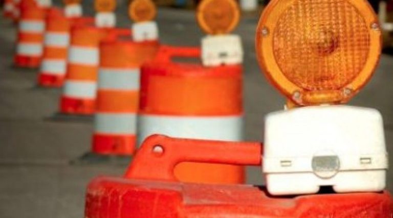 A line of orange and white construction barrels with orange lights on top