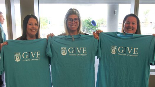 Three women holding up t-shirts