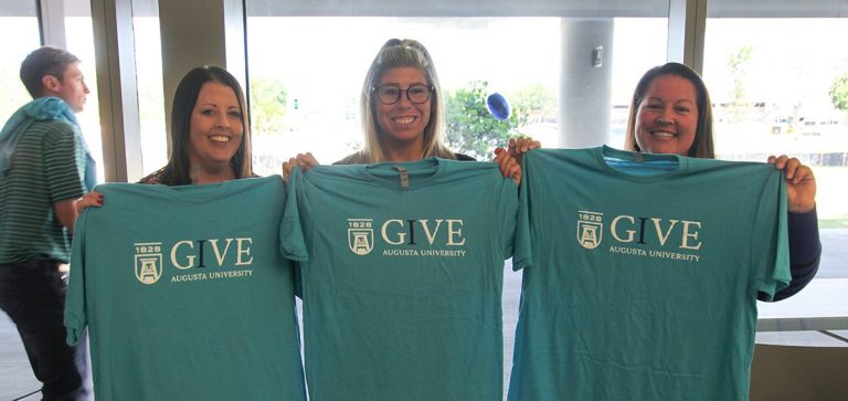 Three women holding up t-shirts