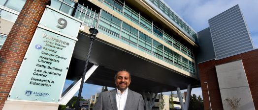 a doctor standing in front of the Georgia Cancer Center building.