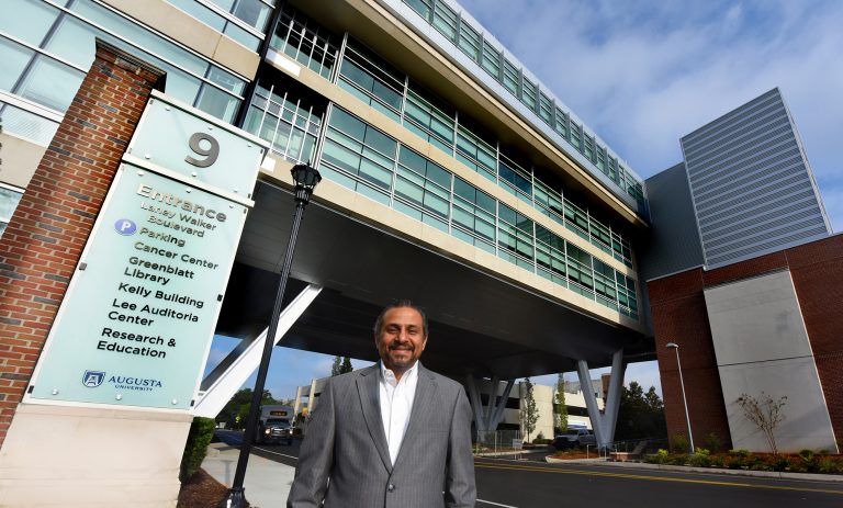 a doctor standing in front of the Georgia Cancer Center building.
