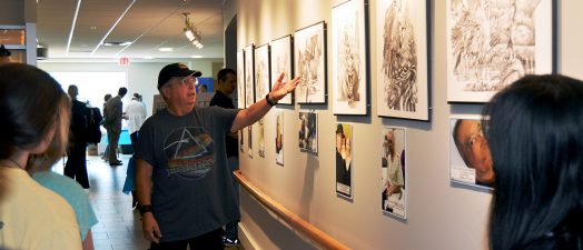 Man standing in front of sketches hanging on the wall.