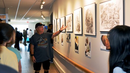 Man standing in front of sketches hanging on the wall.