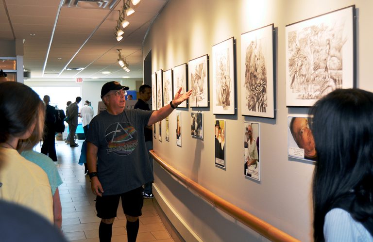 Man standing in front of sketches hanging on the wall.
