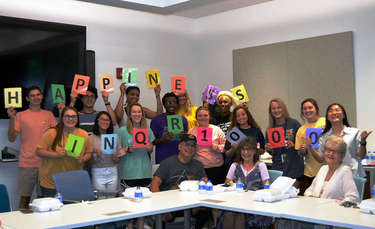 Students, an artist and the artist's wife holding up letters that spell happiness