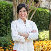 Color photo of woman standing in front of trees and orange flowers