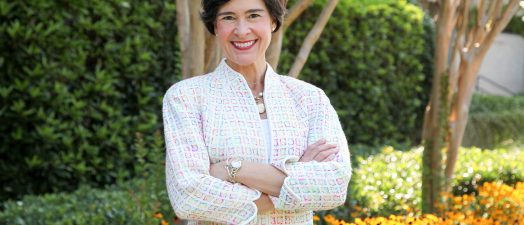 Color photo of woman standing in front of trees and orange flowers