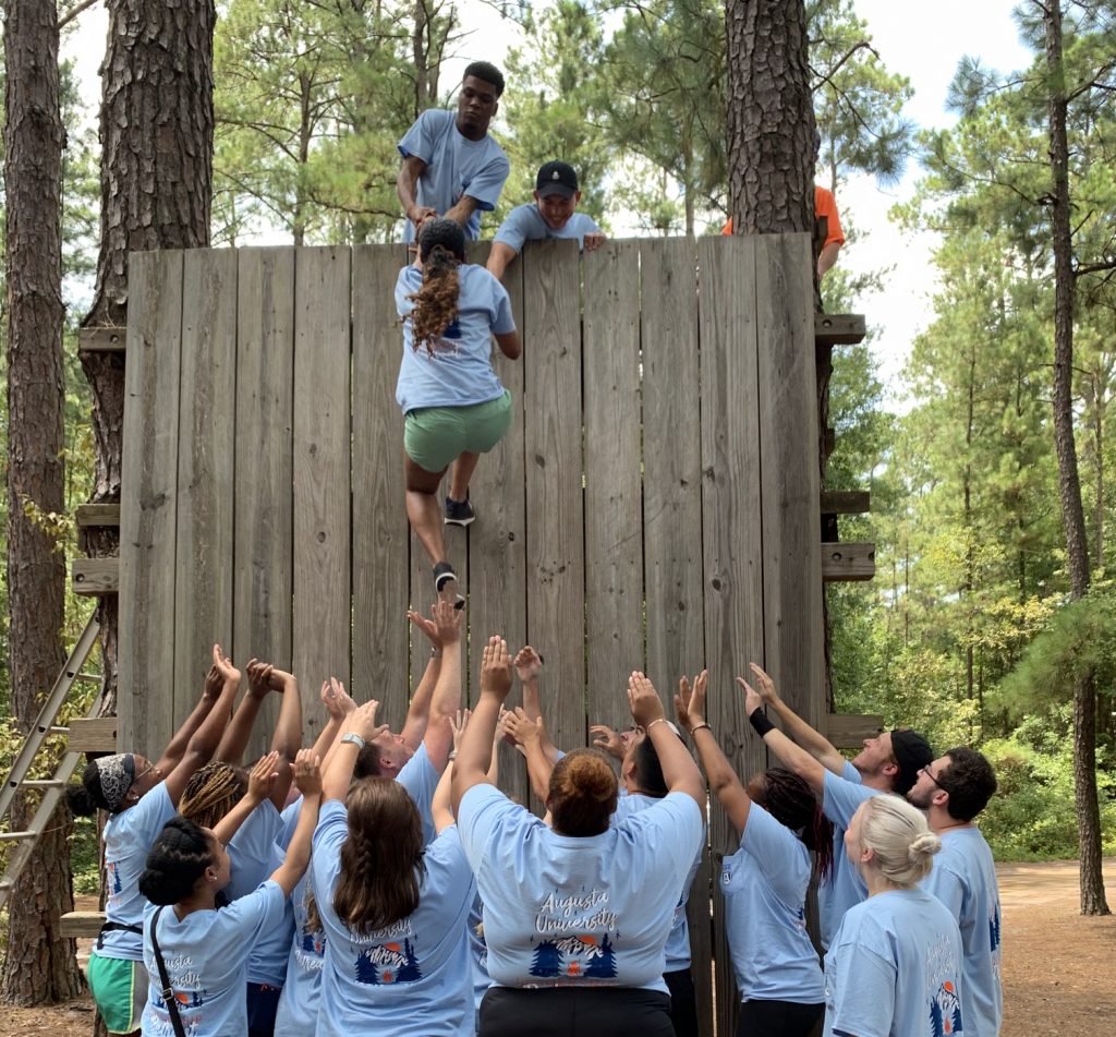 Female student climbs wall with help of two male students