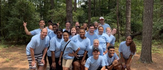 Students and staff members standing on wooden platform, smiling for camera