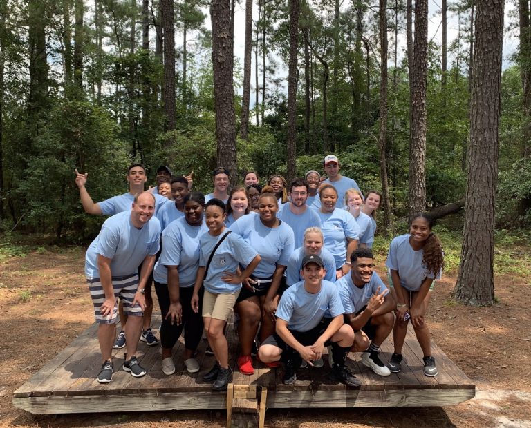 Students and staff members standing on wooden platform, smiling for camera