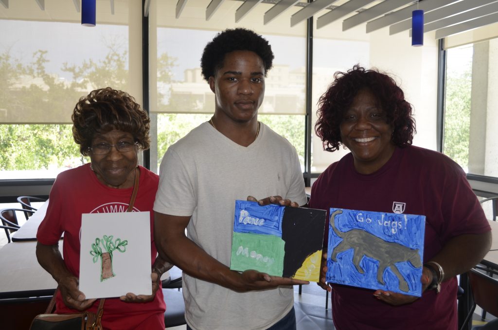 A family of three holding up paintings