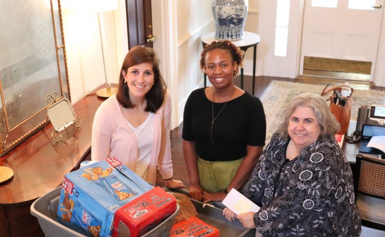 Three women standing over a cart filled with groceries.
