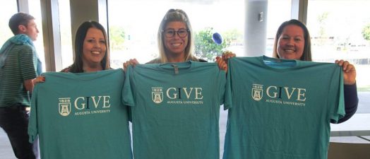Three ladies holding up shirts.