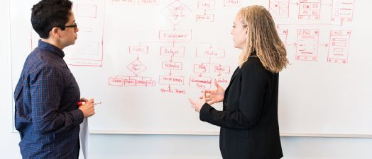 two students writing on the whiteboard.