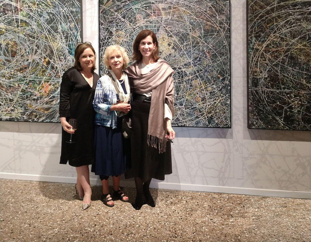 Three women standing in front of paintings.