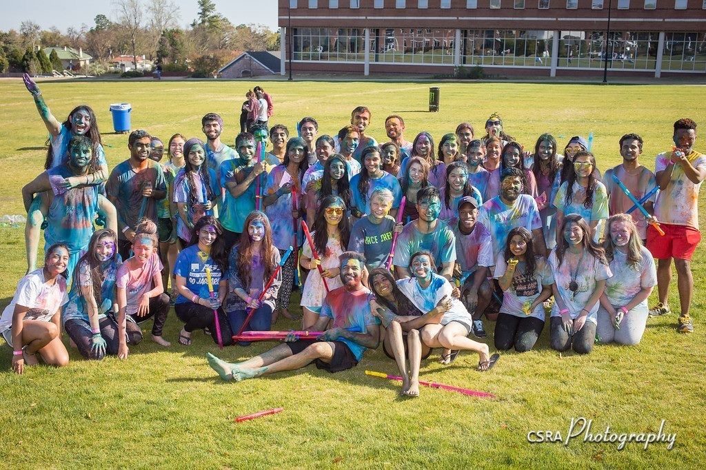 Large group of students covered in color powder, posing for photo on lawn