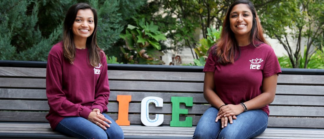 Two female students sitting on a bench in matching club T-shirts.