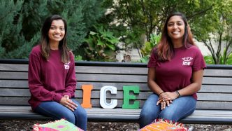 Two female students sitting on a bench in matching club T-shirts.