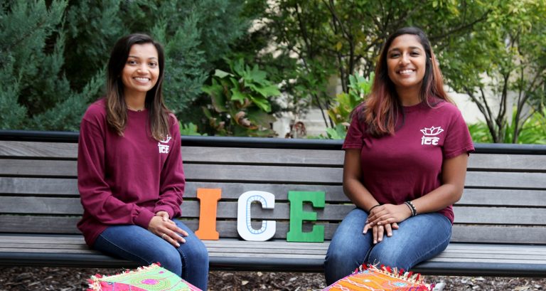 Two female students sitting on a bench in matching club T-shirts.