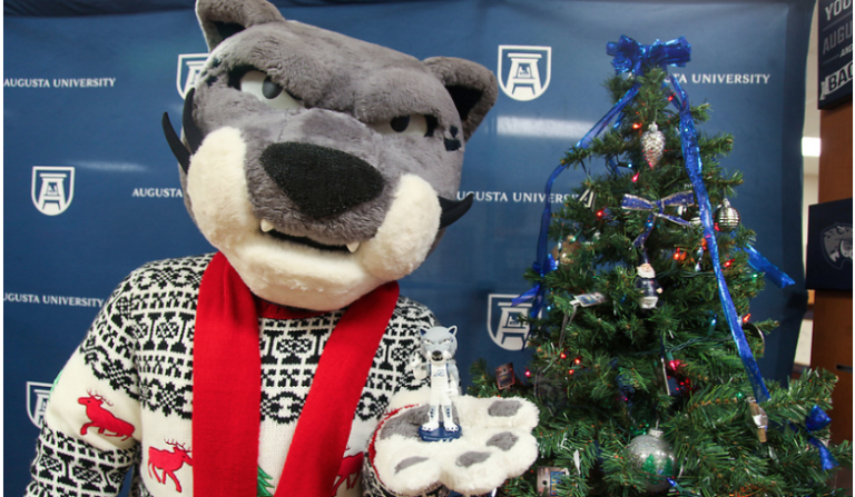 Augustus the mascot standing next to a Christmas tree