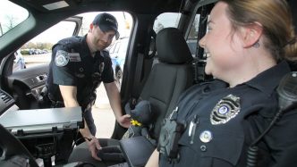 A male and female officers sitting in a cop car.