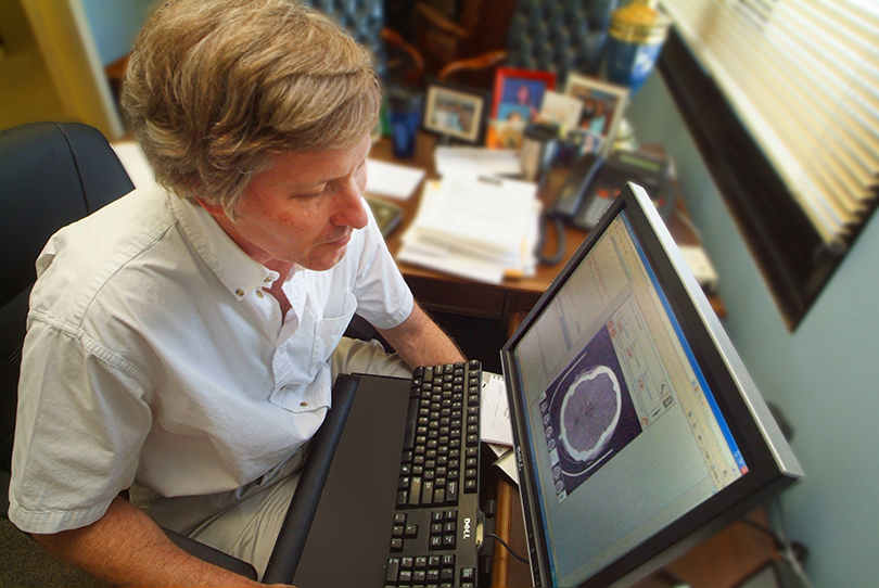 A man sitting in front of a computer looking at an image of a brain.