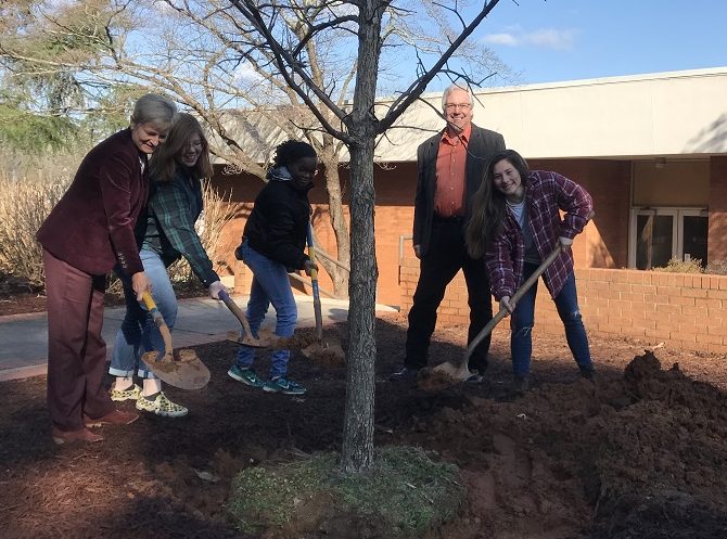 five people shovel dirt on tree