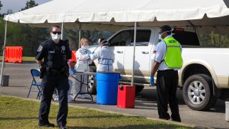 nurses in protective suits with car