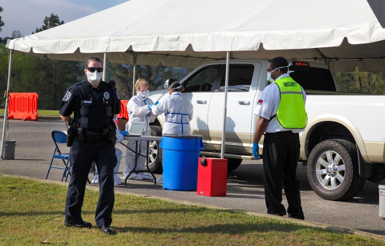 nurses in protective suits with car