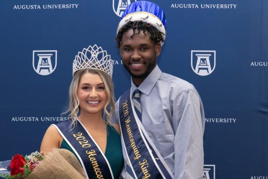 man and woman smiling for photo, wearing crowns and sashes