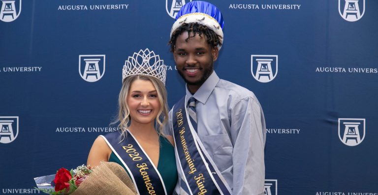 man and woman smiling for photo, wearing crowns and sashes