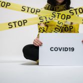 person wrapped in a sign that says stop holding another sign that reads COVID19