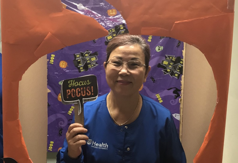 woman in blue scrubs holding sign that says Hocus Pocus