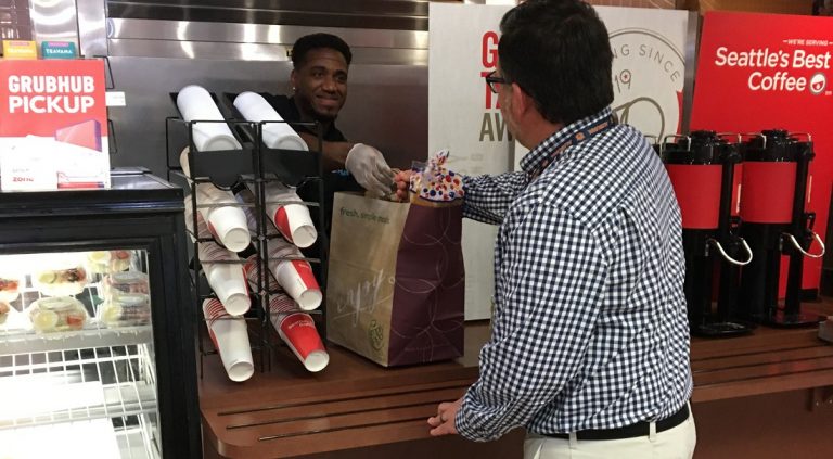 Man reaching across counter for grocery brown bag