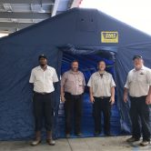 Four men stand at large blue tent