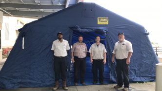 Four men stand at large blue tent