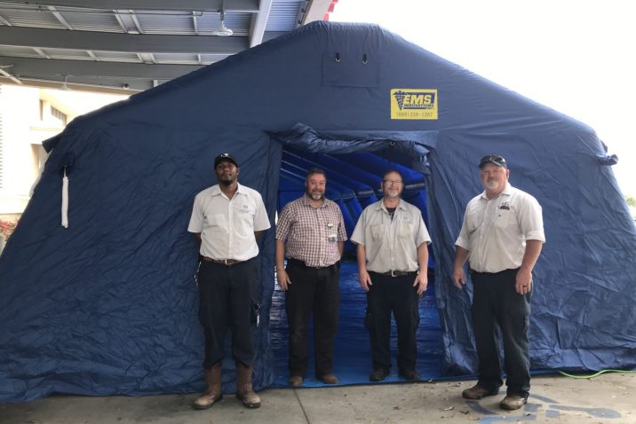 Four men stand at large blue tent