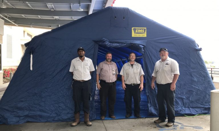 Four men stand at large blue tent